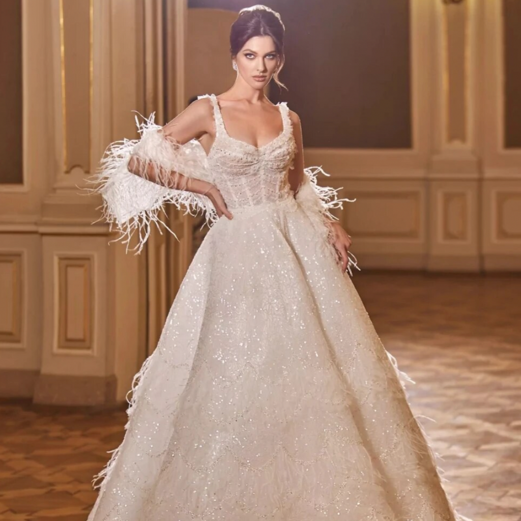 Make your wedding day even more special with our Dress Augustine. This romantic sweetheart neck bridal dress is adorned with sparkly sequins and beads, adding a touch of luxury to your look. The feather details give the dress a unique and elegant touch. Walk down the aisle with confidence and grace in this stunning gown.