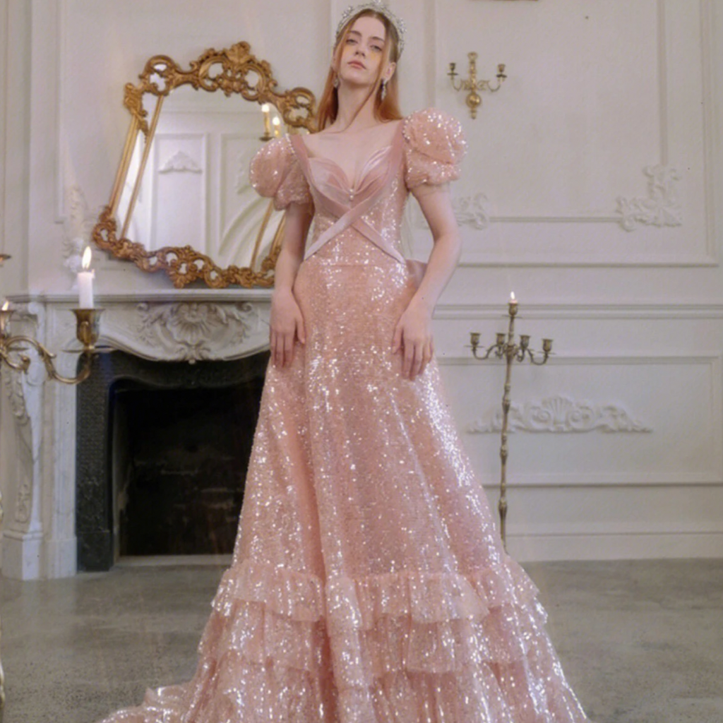 This stunning Robe Kiraz gown is a showstopper. Crafted from soft, lightweight fabric with a sequined bow and pearl zipper, it will instantly elevate your evening wardrobe. Features include a V-neckline, puff sleeves, and a beautiful A-line silhouette in a graceful pink hue. Sparkle and shine all night in this glamorous long glitter fairy gown.