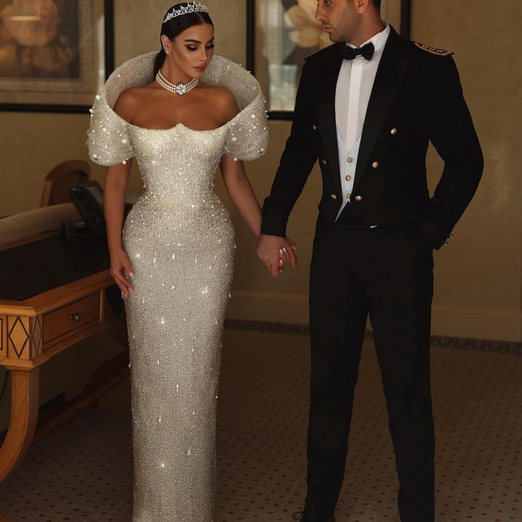 Elevate your wedding elegance with our Dress Alouisa. Custom made with luxurious sequins and pearls, this mermaid dress exudes luxury and grace. The off-the-shoulder design adds a touch of sophistication. Make a statement on your special day with this breathtaking bridal gown.