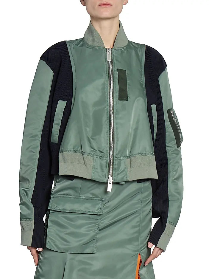 This Nylon Twill Knit Bomber Jacket from Sacai features inset ribbed panels that create a unique striped texture, enhancing its modern cropped blouson silhouette. Designed with a ribbed stand collar and snap cuffs, it combines style with comfort. Practical chest, side, and sleeve zip pockets offer secure storage, while the back vent ensures ease of movement. A two-way front zip closure completes this versatile piece, perfect for elevating your wardrobe with a distinctive, fashion-forward edge.