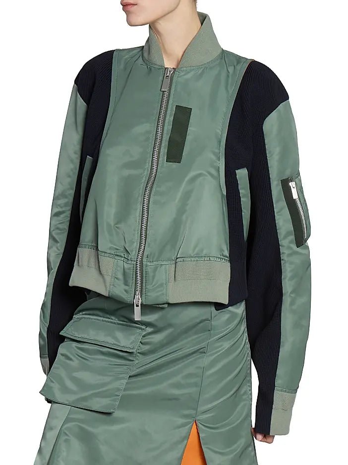 This Nylon Twill Knit Bomber Jacket from Sacai features inset ribbed panels that create a unique striped texture, enhancing its modern cropped blouson silhouette. Designed with a ribbed stand collar and snap cuffs, it combines style with comfort. Practical chest, side, and sleeve zip pockets offer secure storage, while the back vent ensures ease of movement. A two-way front zip closure completes this versatile piece, perfect for elevating your wardrobe with a distinctive, fashion-forward edge.