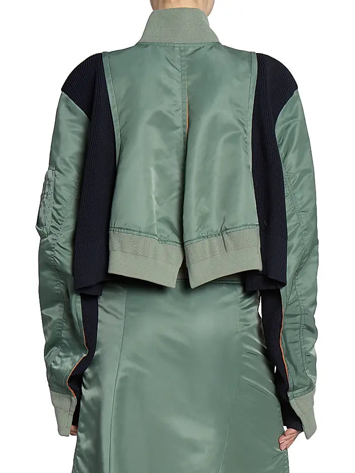 This Nylon Twill Knit Bomber Jacket from Sacai features inset ribbed panels that create a unique striped texture, enhancing its modern cropped blouson silhouette. Designed with a ribbed stand collar and snap cuffs, it combines style with comfort. Practical chest, side, and sleeve zip pockets offer secure storage, while the back vent ensures ease of movement. A two-way front zip closure completes this versatile piece, perfect for elevating your wardrobe with a distinctive, fashion-forward edge.