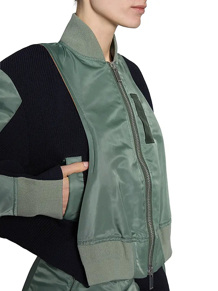 This Nylon Twill Knit Bomber Jacket from Sacai features inset ribbed panels that create a unique striped texture, enhancing its modern cropped blouson silhouette. Designed with a ribbed stand collar and snap cuffs, it combines style with comfort. Practical chest, side, and sleeve zip pockets offer secure storage, while the back vent ensures ease of movement. A two-way front zip closure completes this versatile piece, perfect for elevating your wardrobe with a distinctive, fashion-forward edge.