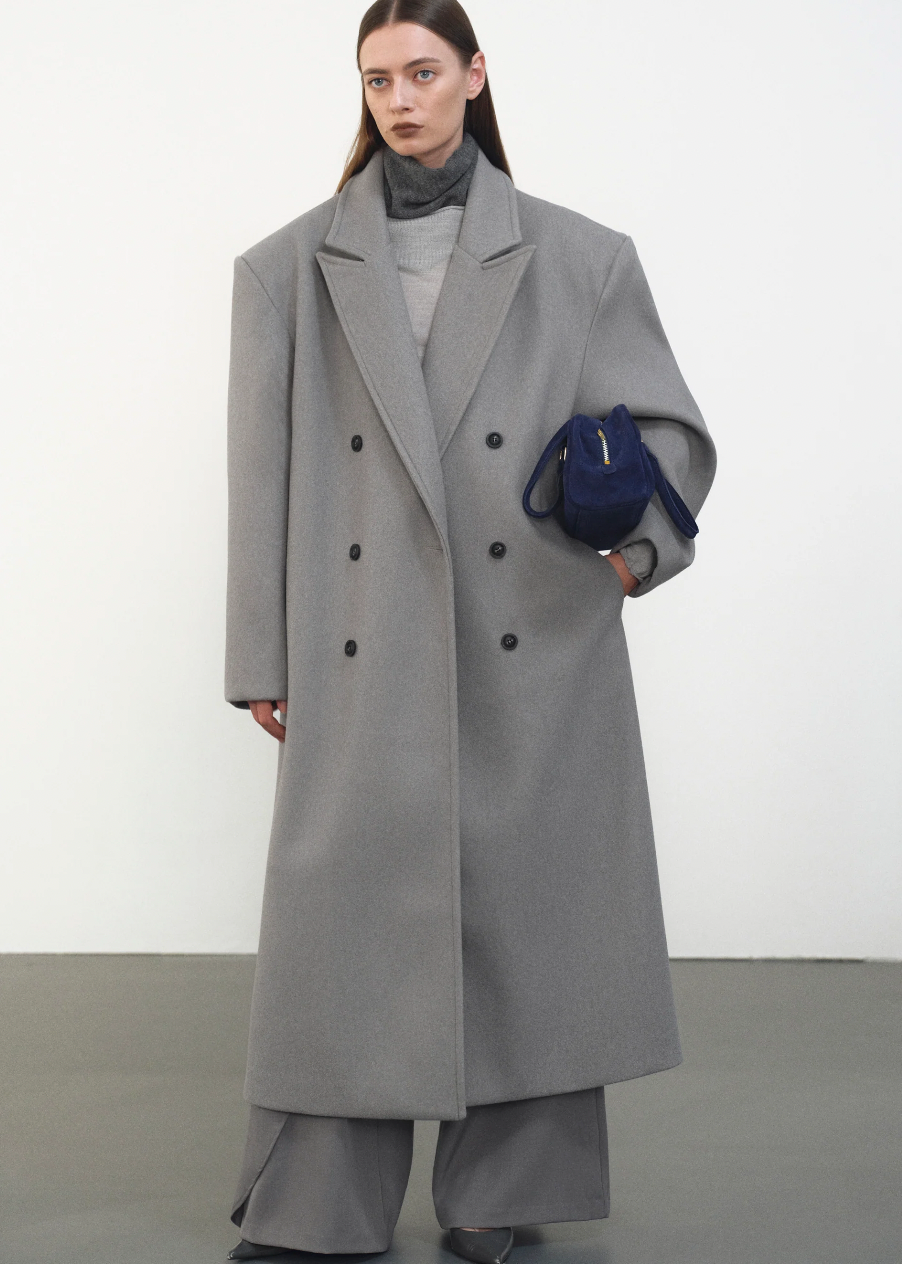Embrace effortless sophistication with the Wallis Oversized Grandpa Coat, a contemporary take on timeless tailoring. Crafted from mid-weight bonded wool-blend fabric, this unisex piece features a dramatically oversized silhouette that commands attention. The striking long peak lapels and double-breasted closure create architectural interest, while structured shoulder pads deliver modern edge. 