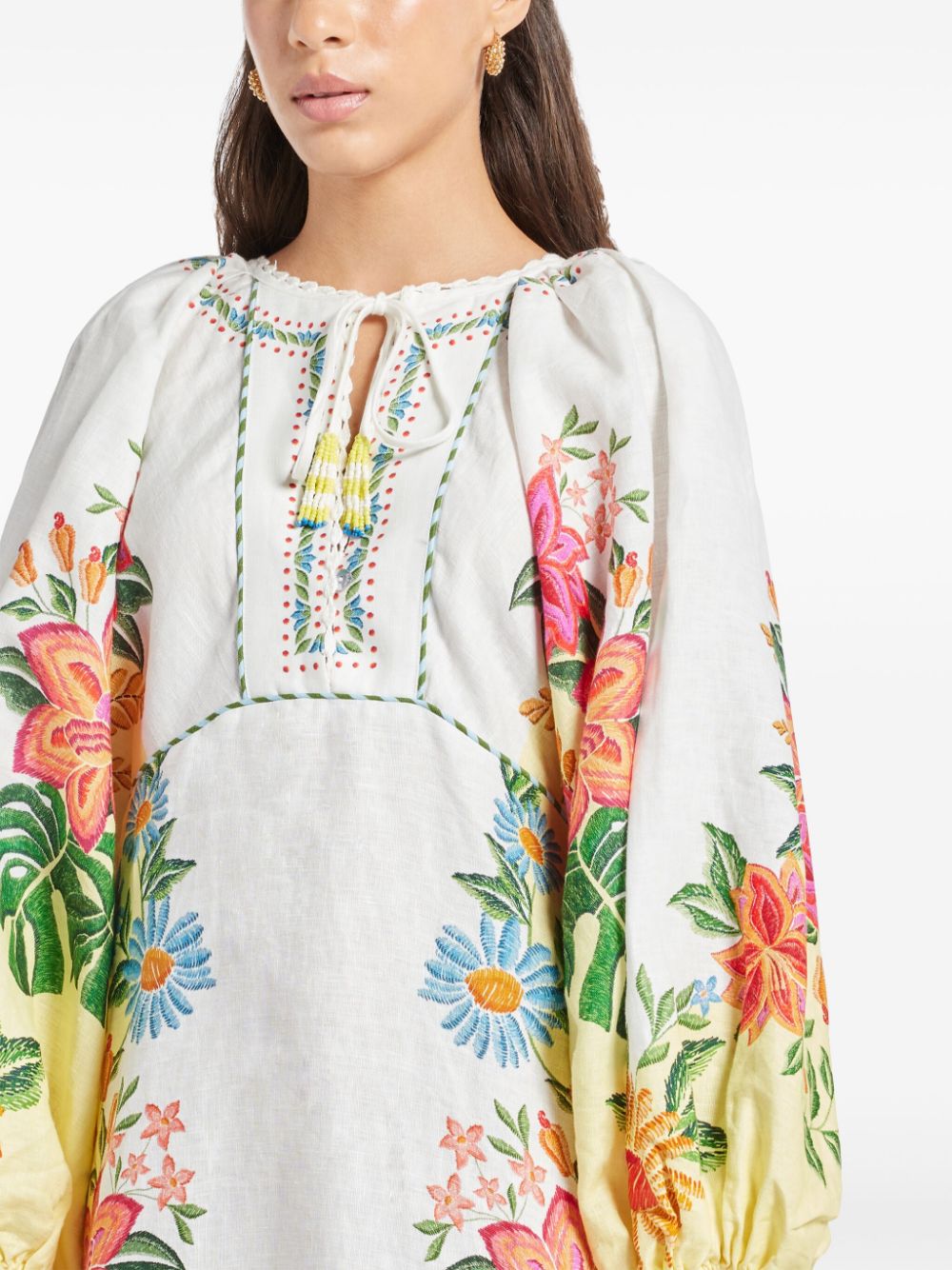 Introducing the Bloom Maxi Dress by FARM Rio. This off-white dress features a beautiful floral print and a unique tassel detail on the neckline. Made with lightweight and breathable linen, the maxi length and elastic cuffs add a playful touch to the elegant design. Complete your summer wardrobe with this must-have piece!