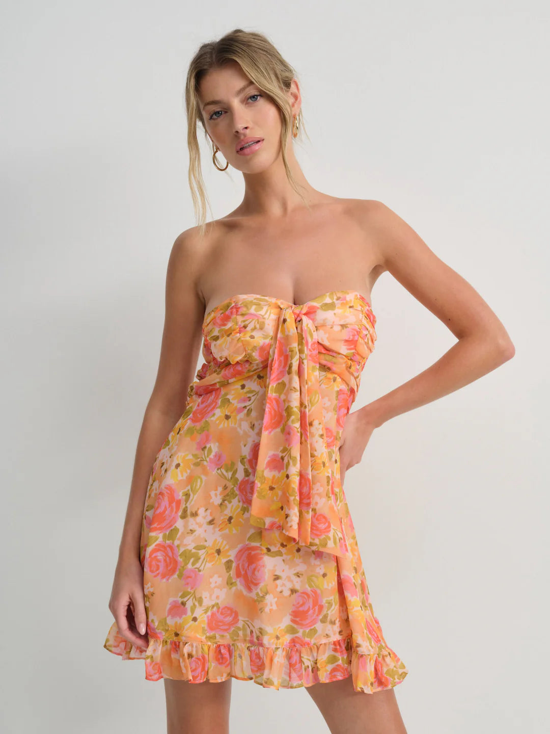Embrace spring romance in the Teagan Mini Dress by For Love and Lemons, a stunning yellow chiffon creation designed to turn heads. This strapless beauty features a delicately gathered bust and charming tie detail that adds movement and personality to every step. Cut to a flirtatious mid-thigh length, it's the perfect balance of elegance and playfulness. Whether you're attending a garden party or enjoying a casual brunch, this floral-inspired piece delivers effortless sophistication with undeniable charm. 