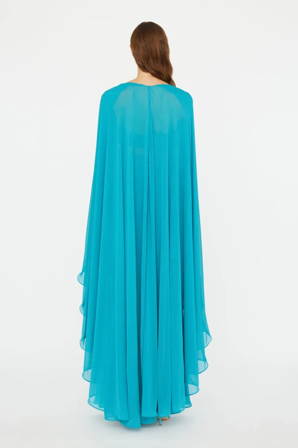 Elevate your wardrobe with the Gyre Cape Effect Dress by Christopher Esber. Crafted from soft jersey, this vibrant turquoise maxi features a dramatic cape-effect overlay and a sleek bandeau bodice that flows to the floor, enhancing your silhouette with delicate draping. Designed for those who seek effortless elegance, this dress makes a bold statement at any special event, especially when complemented with silver jewelry for a touch of refined sophistication.