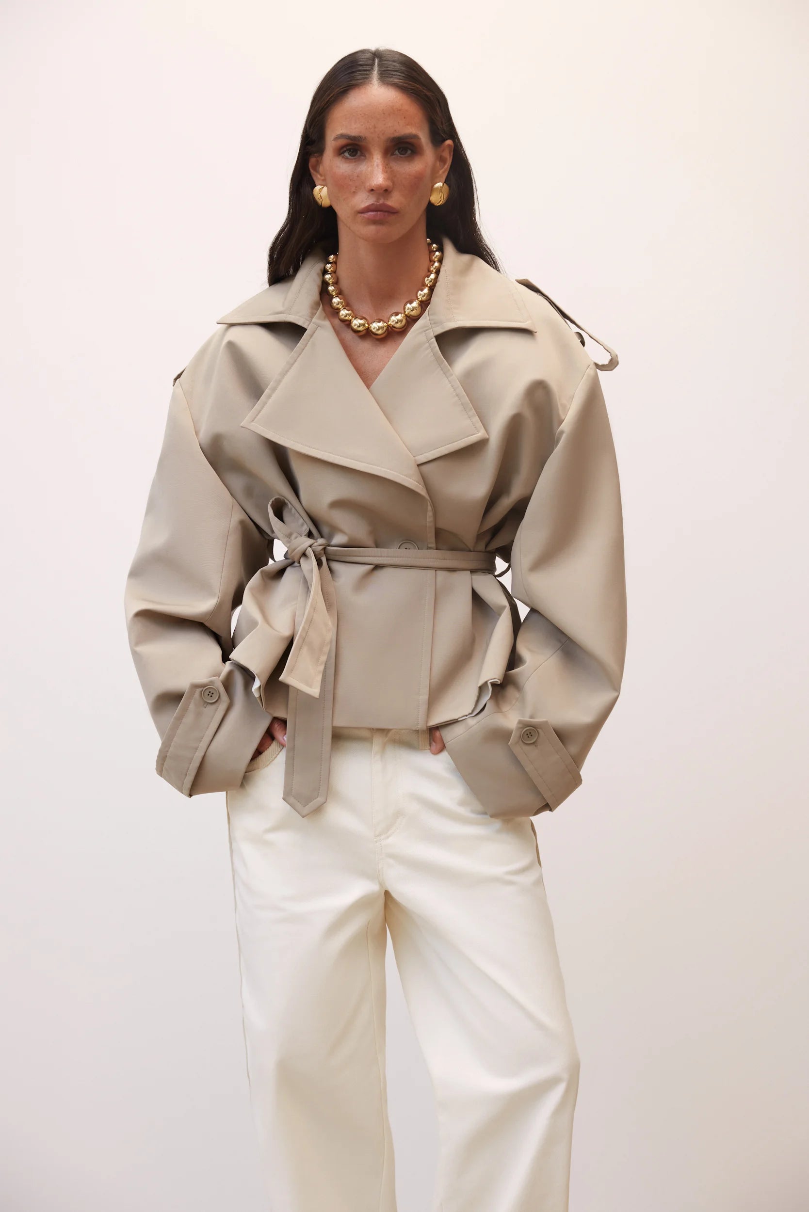 Elevate your wardrobe with this cropped beige trench coat, designed to blend timeless elegance with modern style. Its tailored fit effortlessly complements any outfit, while the neutral beige tone adds versatile sophistication. Ideal for layering, this coat offers both comfort and a chic silhouette, making it a must-have piece for your collection.