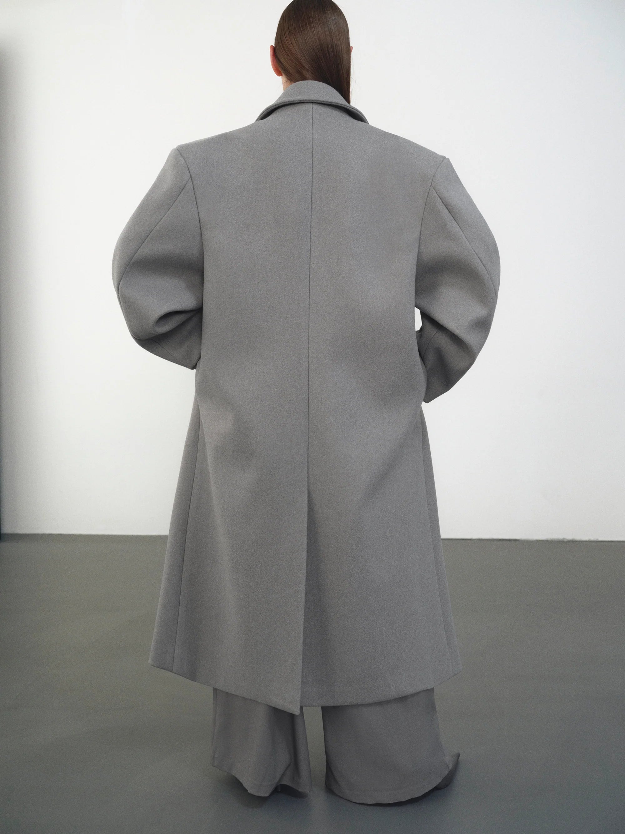 Embrace effortless sophistication with the Wallis Oversized Grandpa Coat, a contemporary take on timeless tailoring. Crafted from mid-weight bonded wool-blend fabric, this unisex piece features a dramatically oversized silhouette that commands attention. The striking long peak lapels and double-breasted closure create architectural interest, while structured shoulder pads deliver modern edge. 