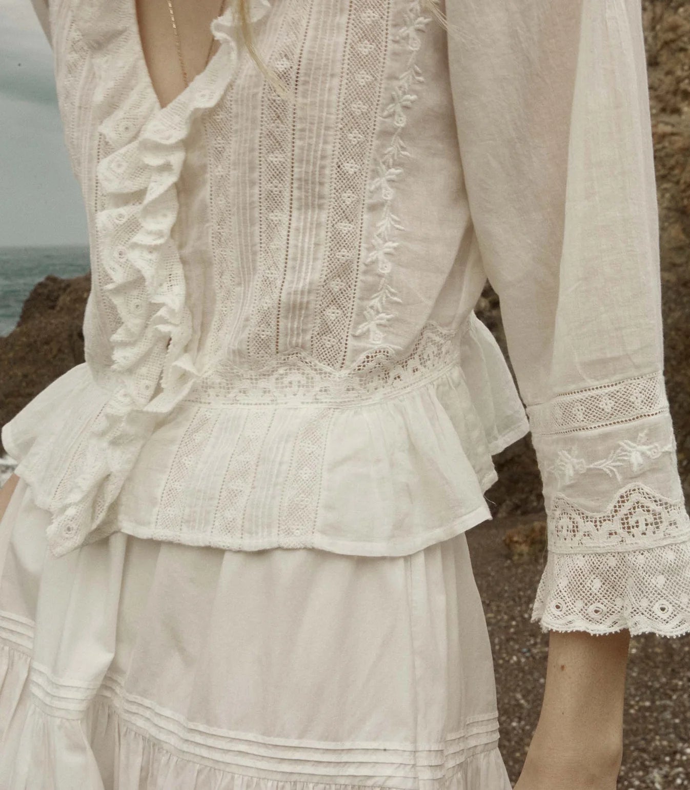 Crafted from the softest organic cotton voile, the Victorian-inspired Eldoris Top features a plunging V-neckline framed with cascading lace-trimmed ruffles that extend down the bodice and alternating panels of inset lace, clustered pintucks, and intricate embroidery at the yoke and back. A line of delicate buttons run down the front, while a cinched and slightly cropped waist finishes in a subtle peplum.