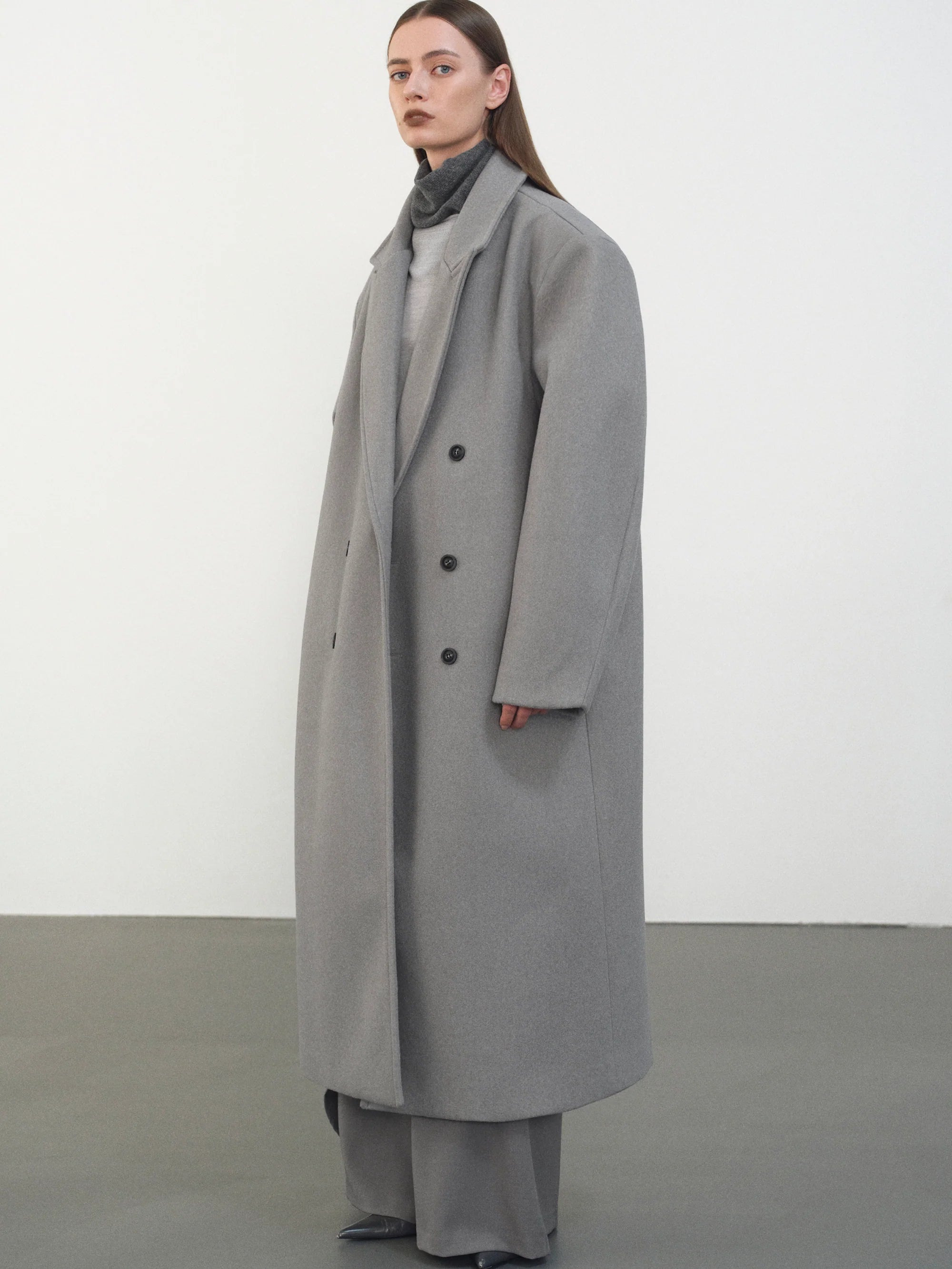 Embrace effortless sophistication with the Wallis Oversized Grandpa Coat, a contemporary take on timeless tailoring. Crafted from mid-weight bonded wool-blend fabric, this unisex piece features a dramatically oversized silhouette that commands attention. The striking long peak lapels and double-breasted closure create architectural interest, while structured shoulder pads deliver modern edge. 