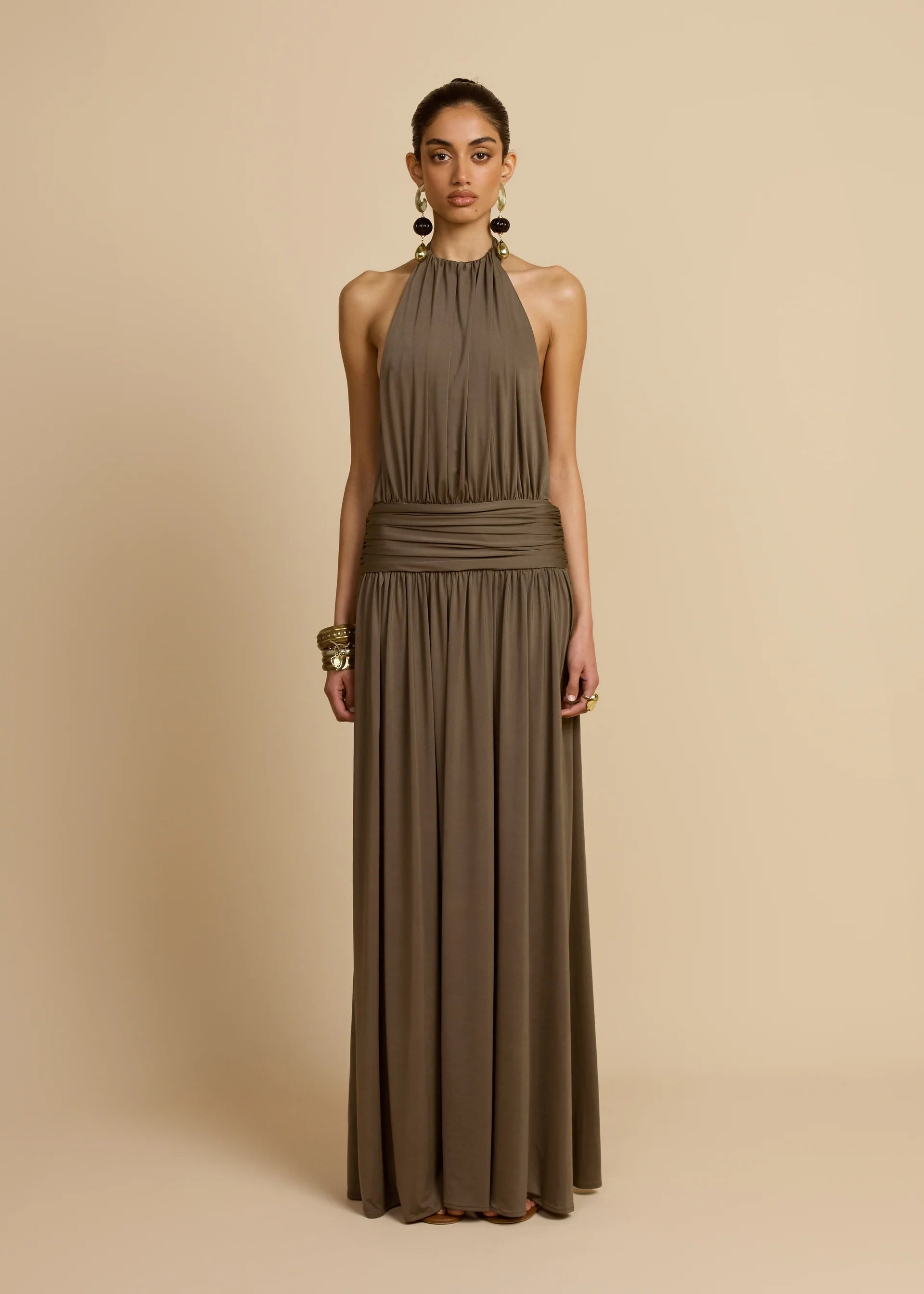 Introducing Santina by Arcina Ori—where sophistication meets movement. This khaki halter dress captivates with its fluid draping and sensual design details, including a ruched centre back and strategically placed gathers that flatter your silhouette. The low-set waistband and floor-length hem create an elongated, graceful line, while the open back design adds an element of allure perfect for making an entrance. 