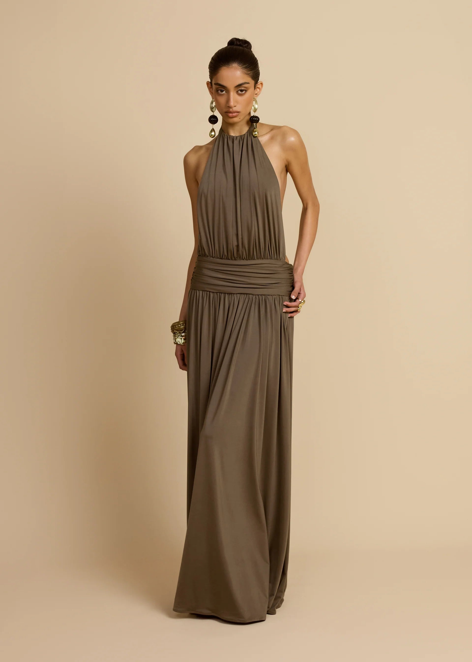 Introducing Santina by Arcina Ori—where sophistication meets movement. This khaki halter dress captivates with its fluid draping and sensual design details, including a ruched centre back and strategically placed gathers that flatter your silhouette. The low-set waistband and floor-length hem create an elongated, graceful line, while the open back design adds an element of allure perfect for making an entrance. 