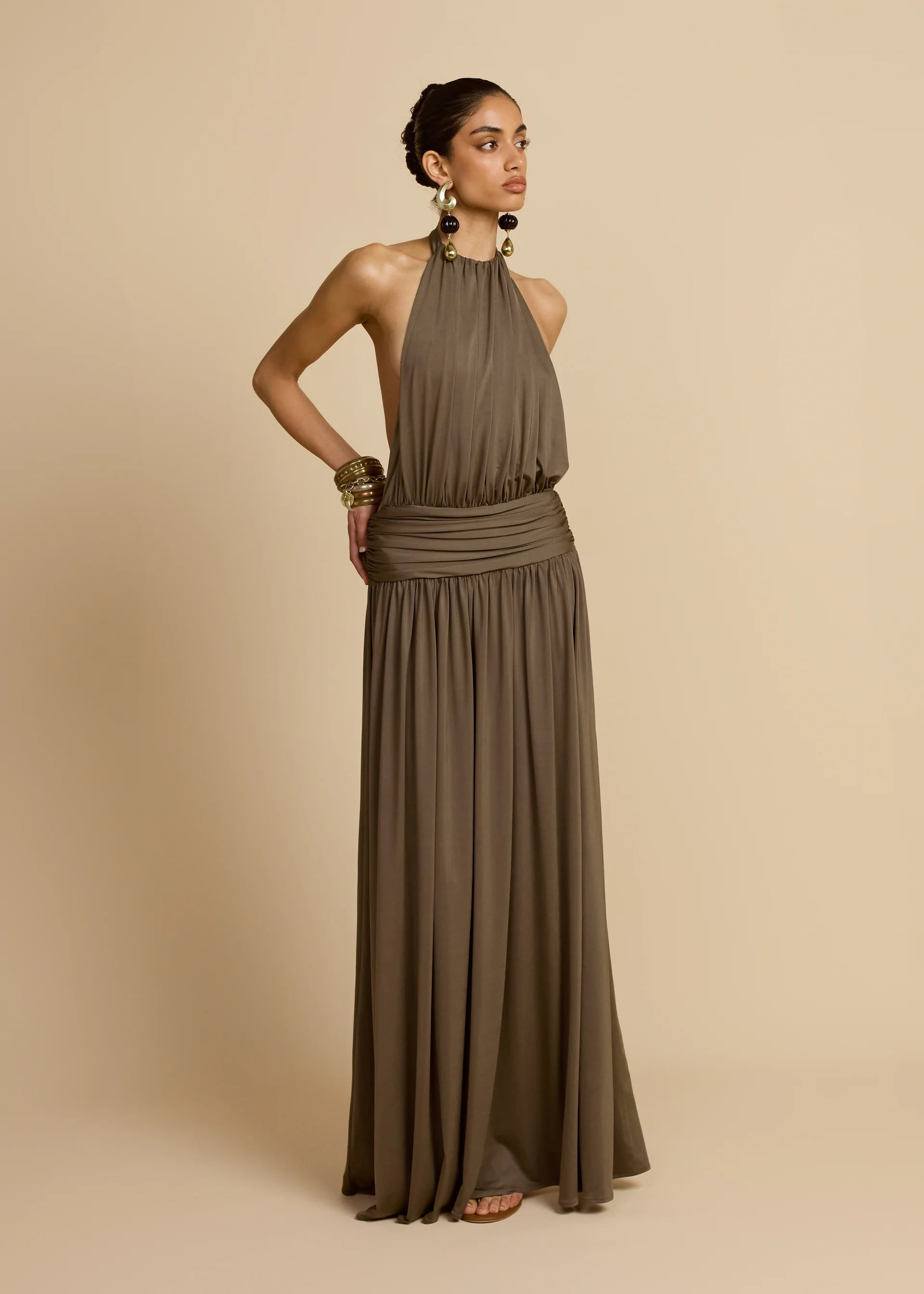 Introducing Santina by Arcina Ori—where sophistication meets movement. This khaki halter dress captivates with its fluid draping and sensual design details, including a ruched centre back and strategically placed gathers that flatter your silhouette. The low-set waistband and floor-length hem create an elongated, graceful line, while the open back design adds an element of allure perfect for making an entrance. 