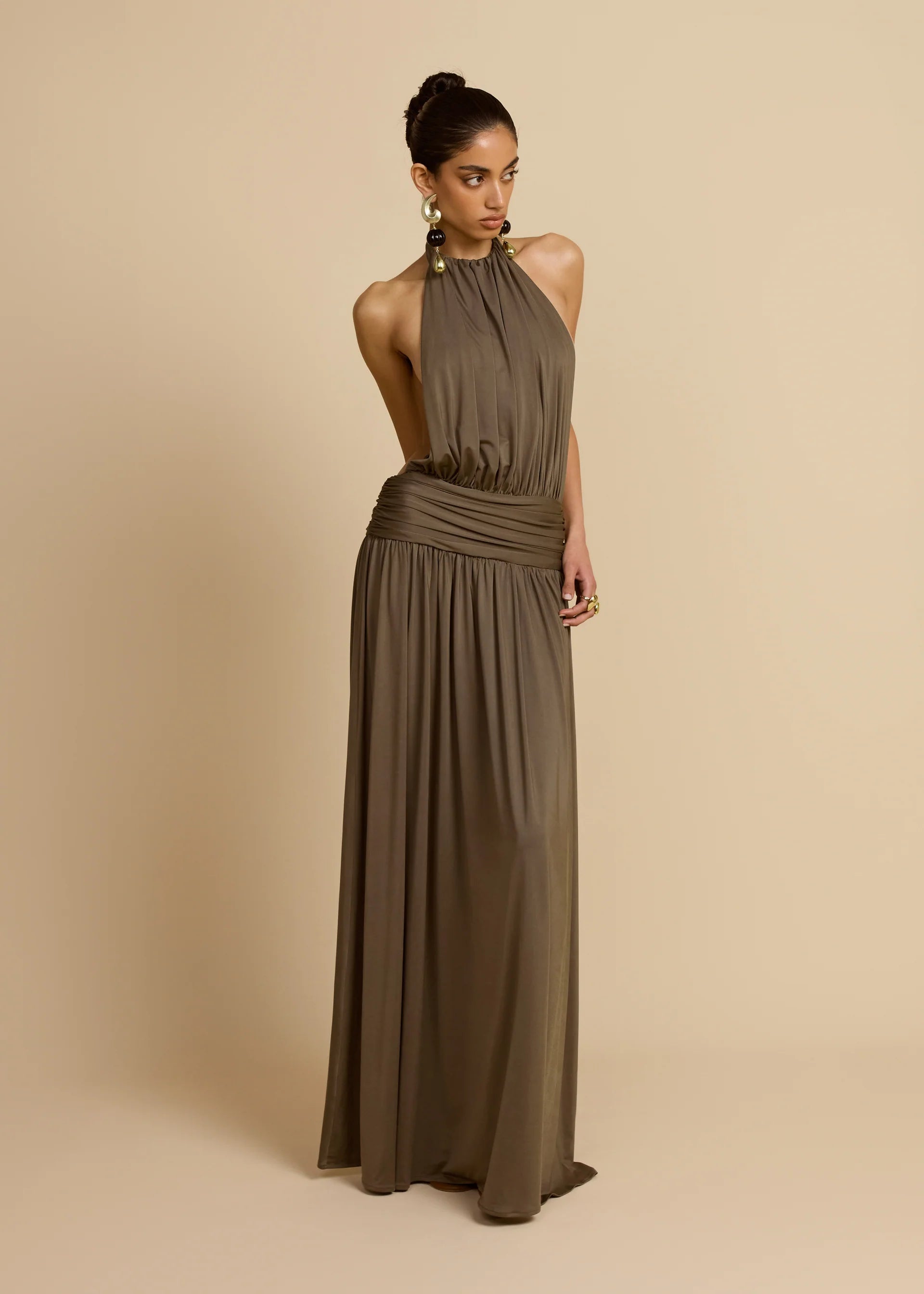 Introducing Santina by Arcina Ori—where sophistication meets movement. This khaki halter dress captivates with its fluid draping and sensual design details, including a ruched centre back and strategically placed gathers that flatter your silhouette. The low-set waistband and floor-length hem create an elongated, graceful line, while the open back design adds an element of allure perfect for making an entrance. 