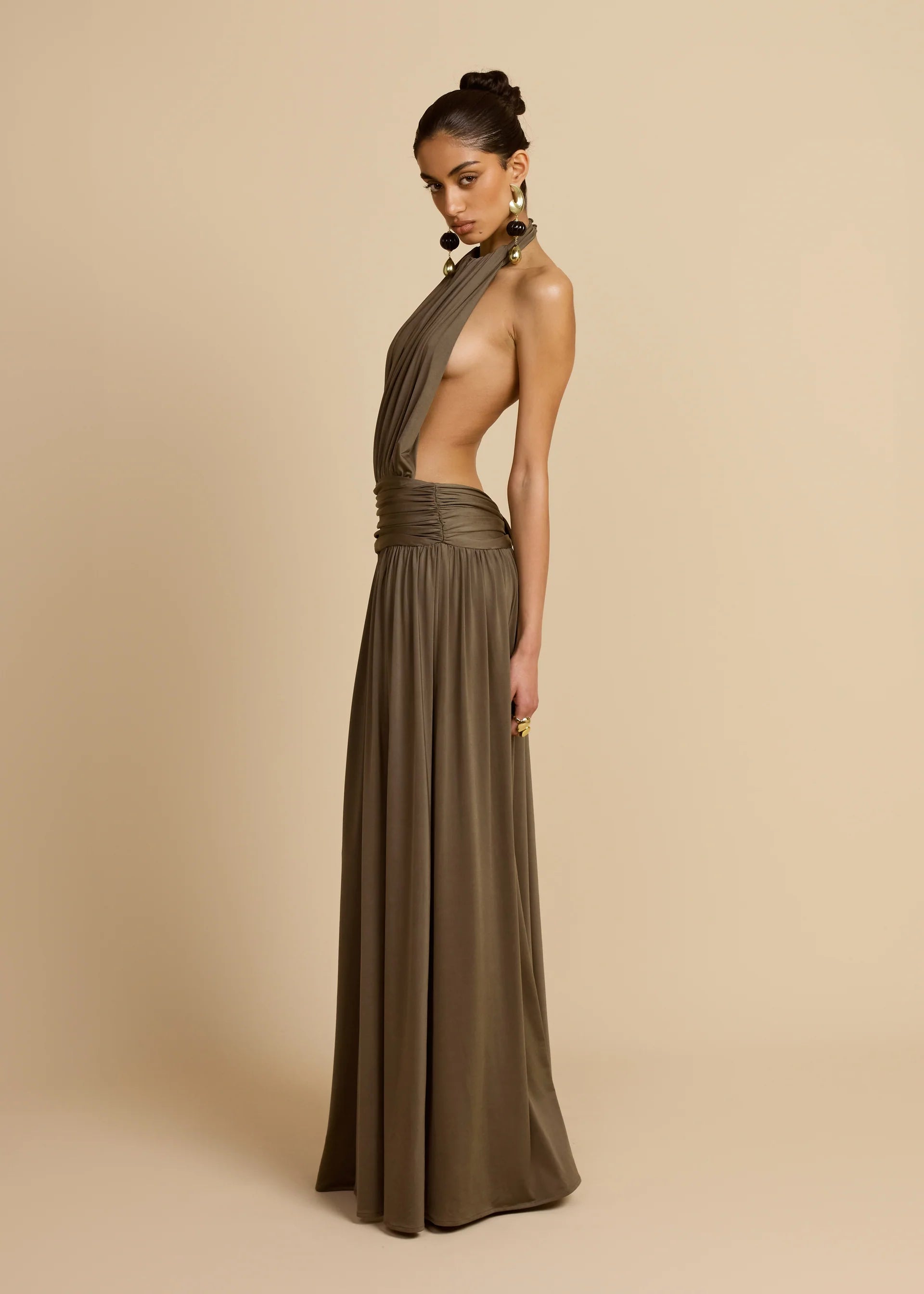Introducing Santina by Arcina Ori—where sophistication meets movement. This khaki halter dress captivates with its fluid draping and sensual design details, including a ruched centre back and strategically placed gathers that flatter your silhouette. The low-set waistband and floor-length hem create an elongated, graceful line, while the open back design adds an element of allure perfect for making an entrance. 