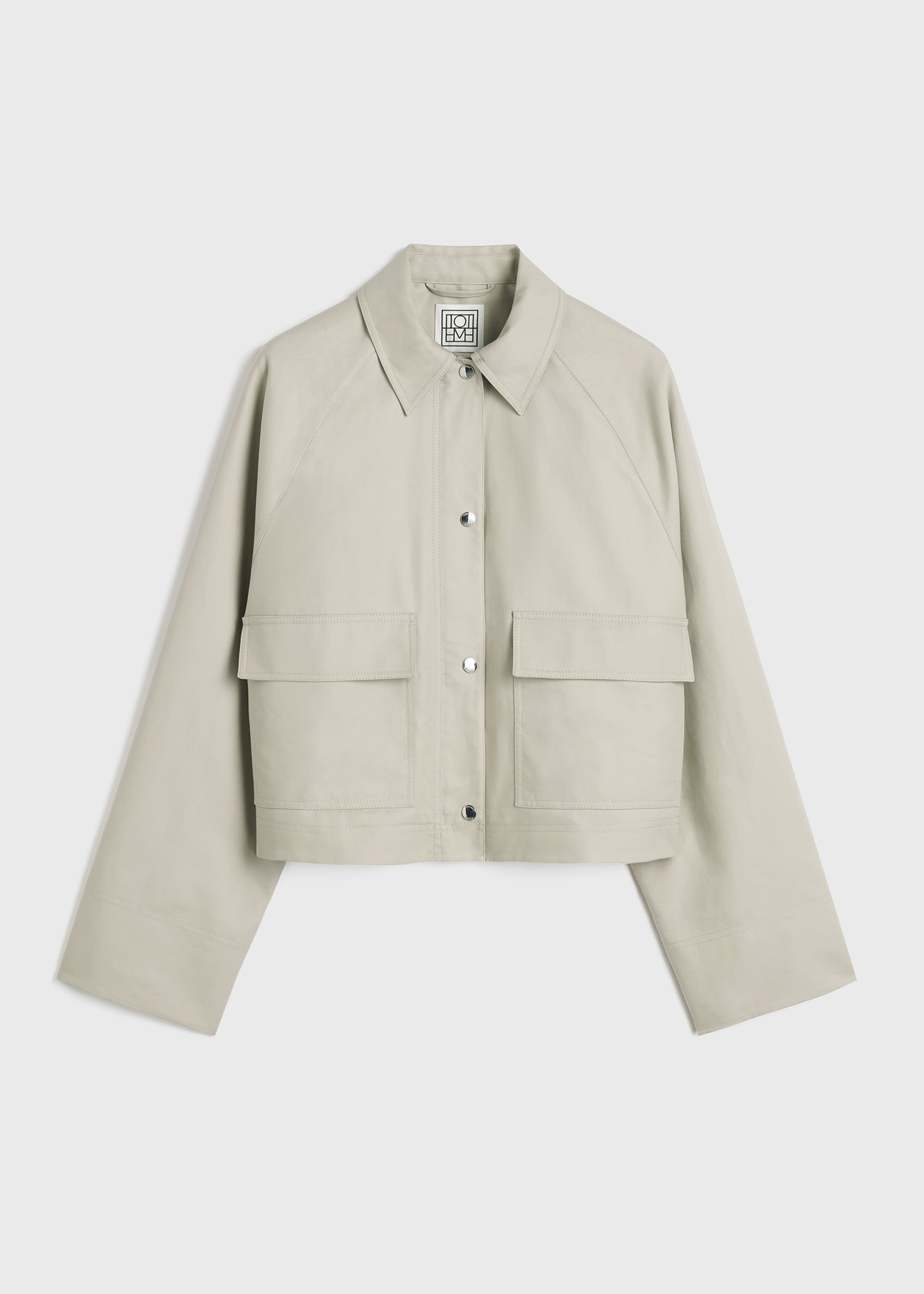 This cropped cotton jacket by Toteme in a warm sand hue features a wide, boxy silhouette with roomy raglan sleeves for a modern, relaxed fit. Crafted from compact organic cotton, it offers durability and comfort. Functional details like a silver-tone zipper, snap buttons, and utilitarian flap pockets add practicality without compromising style. Fully lined in a matching tone, it pairs effortlessly with jeans and pumps, making it the perfect choice for casual coffee outings with a chic edge.