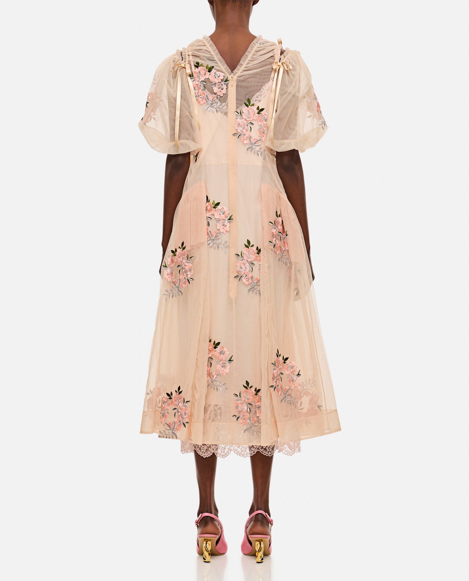 This midi-length dress by Simone Rocha features elegant draped detailing at the waist that flatters your silhouette. Short puff sleeves add a touch of romantic charm, enhanced by delicate applied bows on the shoulders. Embroidered flower accents provide subtle texture and femininity. Designed without a petticoat, the nude-colored fabric offers a smooth, graceful flow perfect for any occasion that demands effortless sophistication.