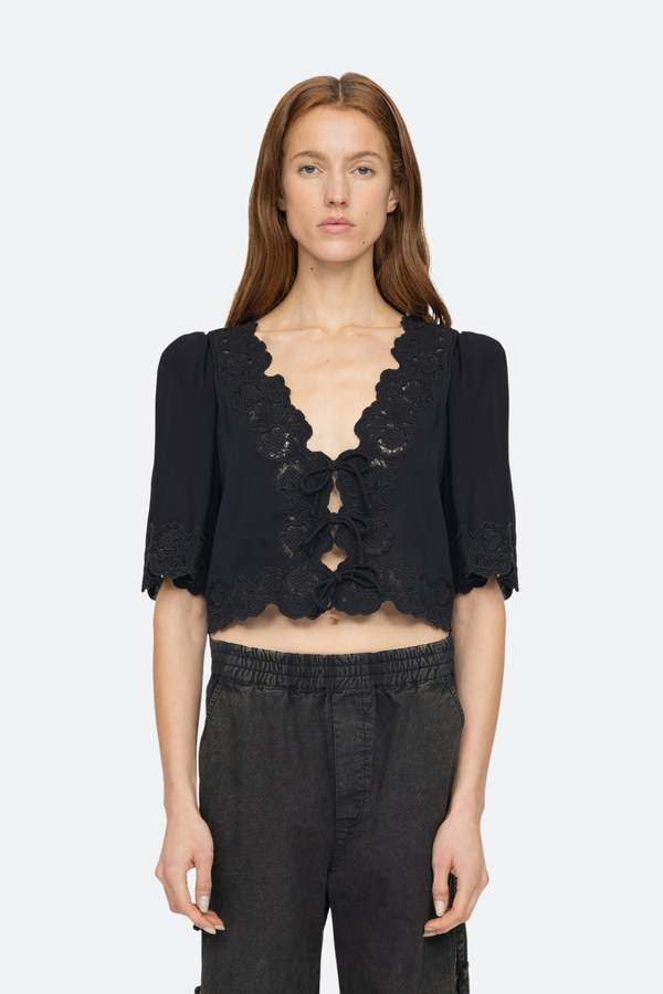 Elevate your wardrobe with the effortlessly elegant Baylin Top in Black by SEA. Delicate lace detailing and front tie closures exude sophistication and charm, while the flowy short sleeves add a touch of femininity. Luxurious and versatile, this top is a must-have for any occasion.