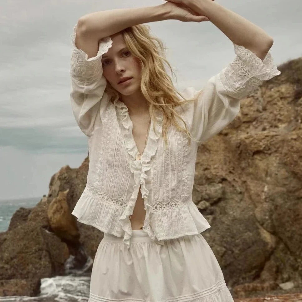 Crafted from the softest organic cotton voile, the Victorian-inspired Eldoris Top features a plunging V-neckline framed with cascading lace-trimmed ruffles that extend down the bodice and alternating panels of inset lace, clustered pintucks, and intricate embroidery at the yoke and back. A line of delicate buttons run down the front, while a cinched and slightly cropped waist finishes in a subtle peplum.