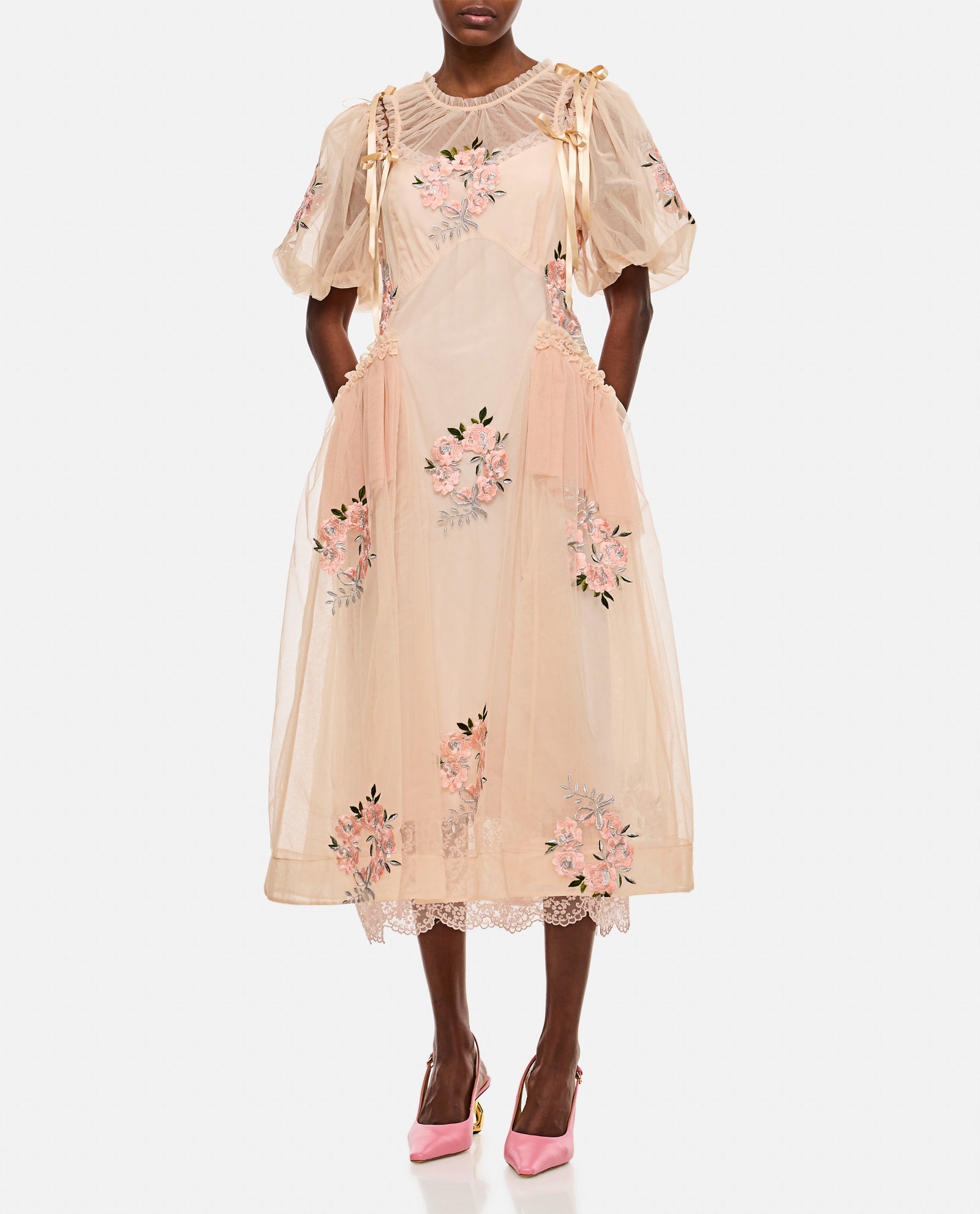 This midi-length dress by Simone Rocha features elegant draped detailing at the waist that flatters your silhouette. Short puff sleeves add a touch of romantic charm, enhanced by delicate applied bows on the shoulders. Embroidered flower accents provide subtle texture and femininity. Designed without a petticoat, the nude-colored fabric offers a smooth, graceful flow perfect for any occasion that demands effortless sophistication.