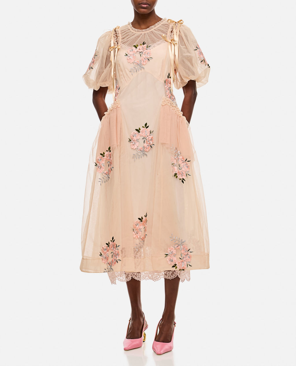 This midi-length dress by Simone Rocha features elegant draped detailing at the waist that flatters your silhouette. Short puff sleeves add a touch of romantic charm, enhanced by delicate applied bows on the shoulders. Embroidered flower accents provide subtle texture and femininity. Designed without a petticoat, the nude-colored fabric offers a smooth, graceful flow perfect for any occasion that demands effortless sophistication.