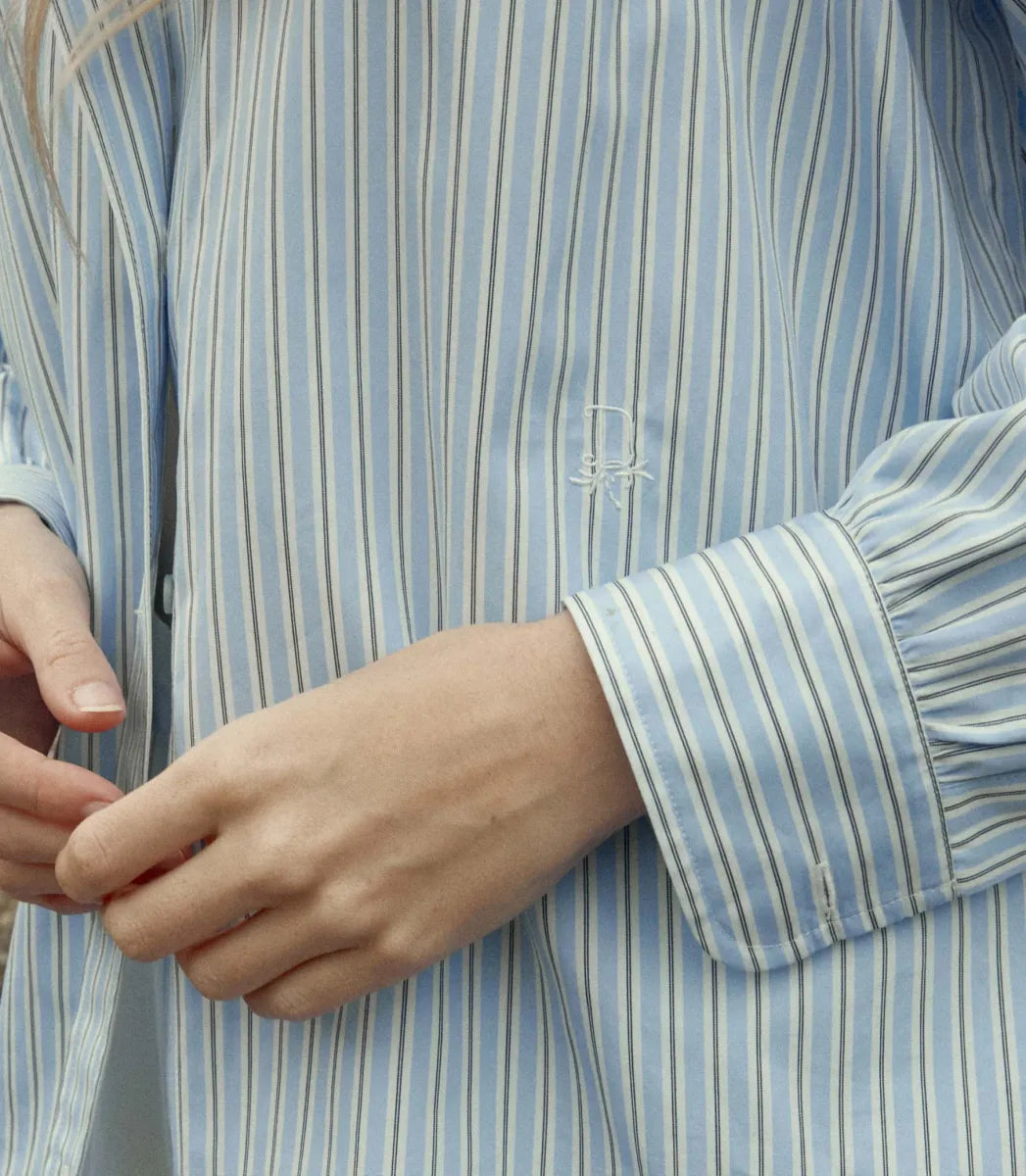 Elevate your wardrobe with the Hava Top in Santorini Stripe by Doen. Made from luxurious Italian cotton, this button-down features a sophisticated Santorini Stripe pattern and mother-of-pearl buttons. The embroidered and shirring details add unique flair to its tailored silhouette, perfect for both casual and polished looks. Versatile and elegant, it's a must-have for any fashion-forward individual.