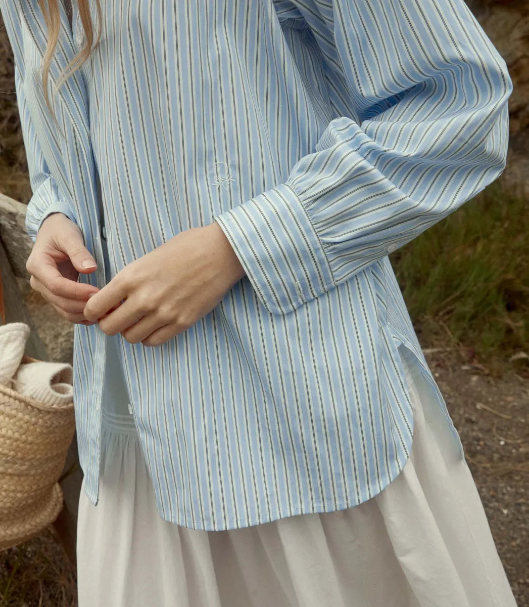 Elevate your wardrobe with the Hava Top in Santorini Stripe by Doen. Made from luxurious Italian cotton, this button-down features a sophisticated Santorini Stripe pattern and mother-of-pearl buttons. The embroidered and shirring details add unique flair to its tailored silhouette, perfect for both casual and polished looks. Versatile and elegant, it's a must-have for any fashion-forward individual.