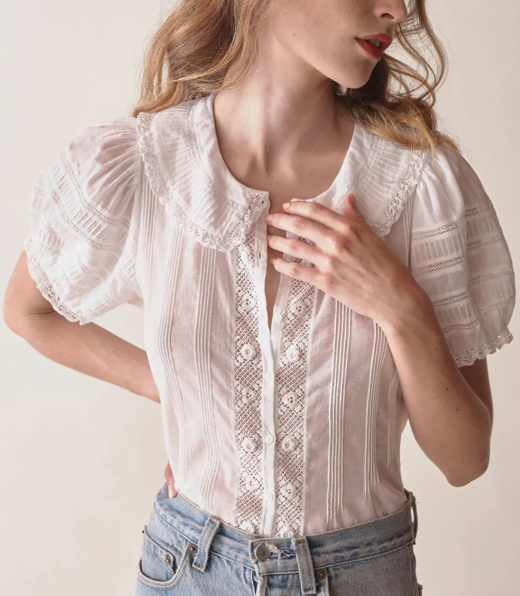 In the softest organic cotton voile, the Bernadine Top by Doen offers a blend of vintage charm and contemporary flair. Featuring a Peter Pan collar and short puffed sleeves adorned with pintucks and inset lace, this slightly cropped blouse is detailed with mother-of-pearl buttons down the front. Delicate scallop-edged butterfly lace trims the collar and sleeve cuffs, enhancing its feminine appeal. Perfect for adding a touch of elegance to any casual ensemble.