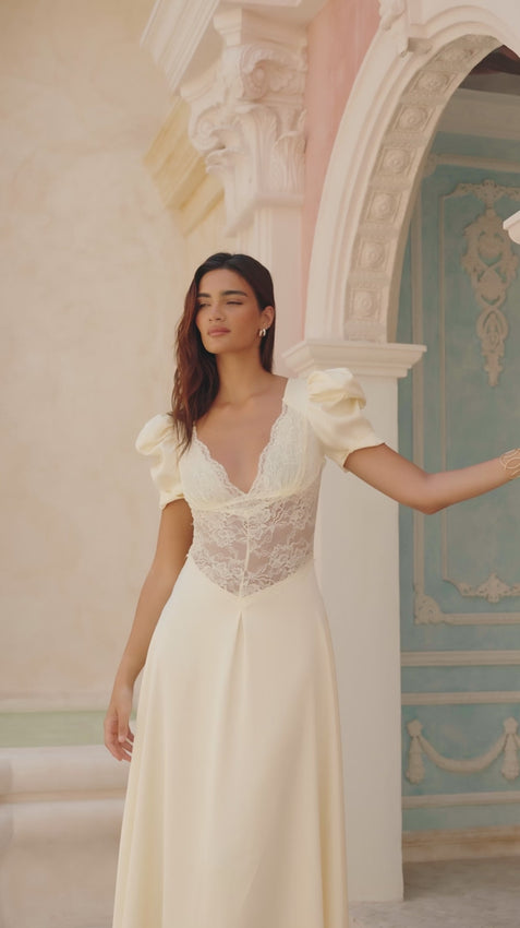 Elegant midi dress in whisper-soft satin, adorned with delicate lace at the bodice. Features a refined V-neckline and romantic puff sleeves that frame the shoulders beautifully. The cinched waist flows into a flowing skirt for an effortlessly graceful silhouette. Perfect for weddings, garden parties, and refined celebrations.
