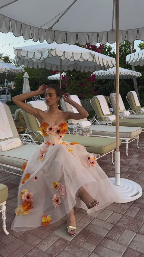 Celebrate timeless elegance with this strapless tea-length gown, where nature's artistry meets refined craftsmanship. Intricate poppy embroidery in warm sunset hues cascades across delicate tulle, while a structured bodice with subtle underwire support provides confident grace. The pairing of horsehair and ethereal tulle creates a silhouette that balances sculptural definition with romantic movement. Rendered in soft Ecru and Poppy tones, this embroidered masterpiece embodies understated sophistication.