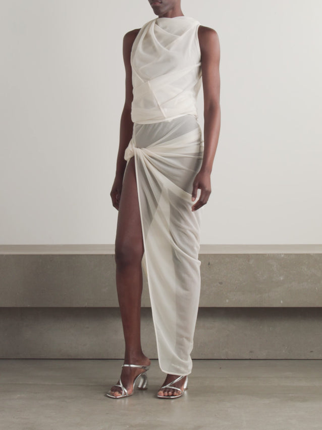 This maxi skirt from Rick Owens features lightweight jersey fabric expertly twisted at the hip to reveal a stylish leg-baring split and graceful drape. The semi-sheer texture offers an alluring look that’s perfectly balanced with tonal underpinnings for elegant coverage. Elevate your wardrobe with this asymmetrical piece that blends comfort and bold design.