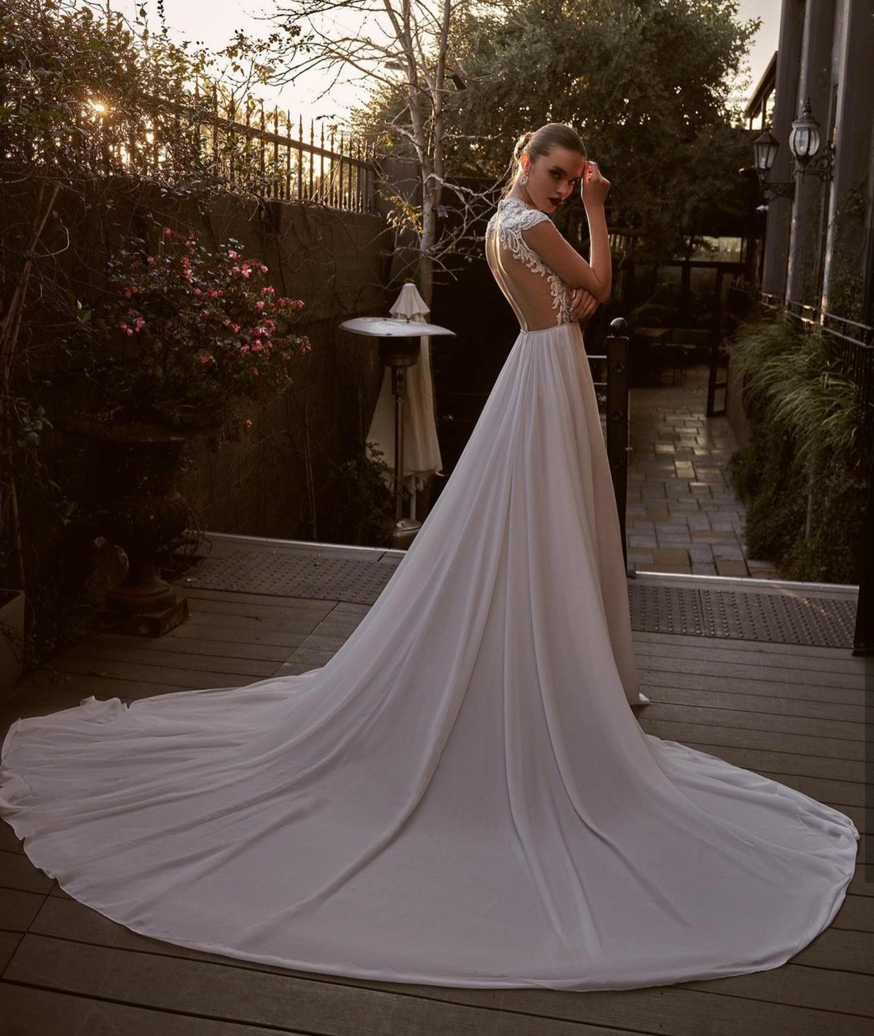 Enhance your special day with the luxurious Robe Lian. This exquisite Wedding Dress features a jewel neckline, delicate lace appliques, and elegant cap sleeves, all crafted with the finest chiffon fabric. The sweeping train and custom fit make this Boho-inspired dress a must-have for the sophisticated bride.