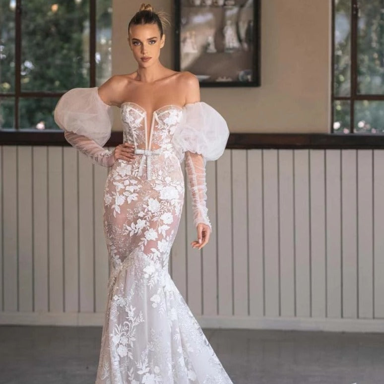 Indulge in the enchanting elegance of the Robe Magda. This stunning dress boasts intricate lace and embroidered flowers adorned with sparkling crystal beading. Its detachable off-the-shoulder puff tulle sleeves add a touch of versatility, while the iconic Berta Bow Belt adds a touch of luxury. Perfect for any special occasion.